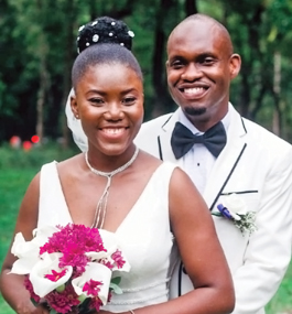 A bride in a white dress holding a bouquet of white and magenta flowers, and a groom in a white suit with his hands around her waist.